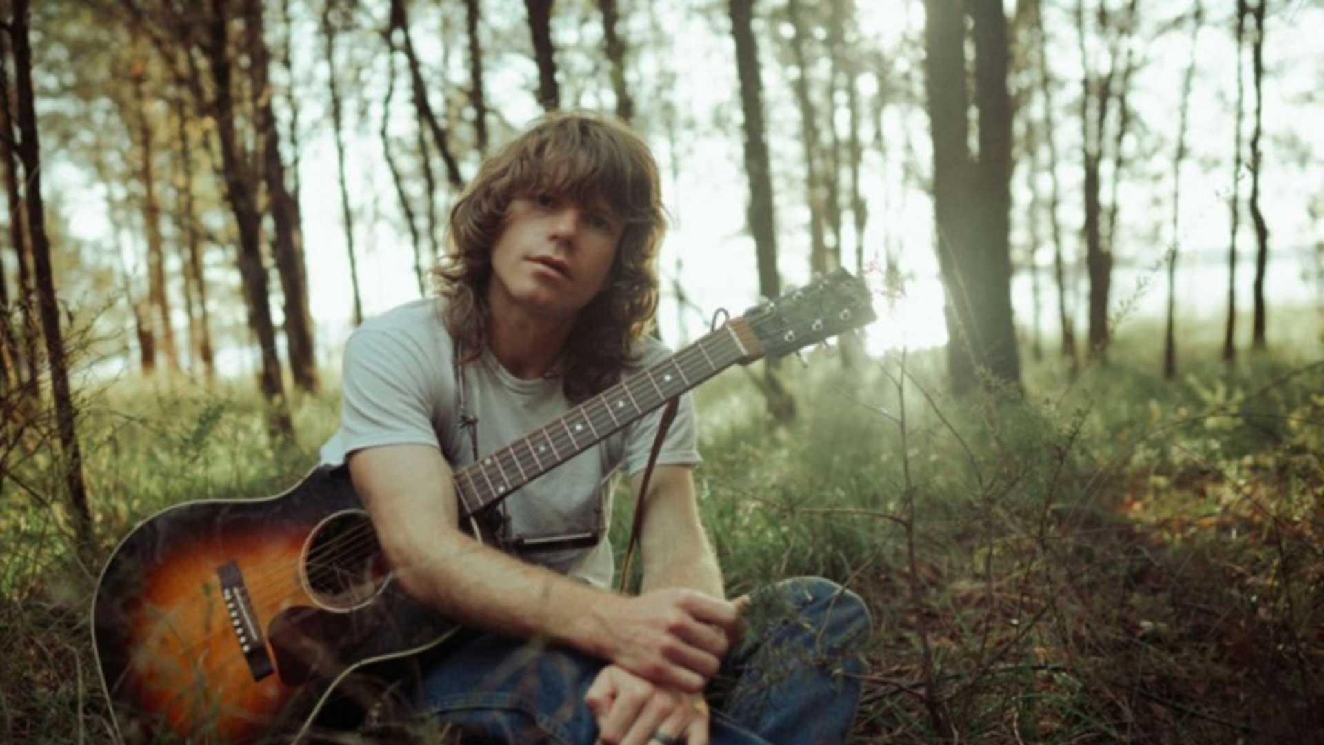 promotional picture of jesse welles with a guitar in the woods