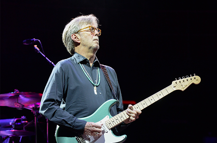 Eric Clapton in een blauw overhemd, gitaar spelend op een podium