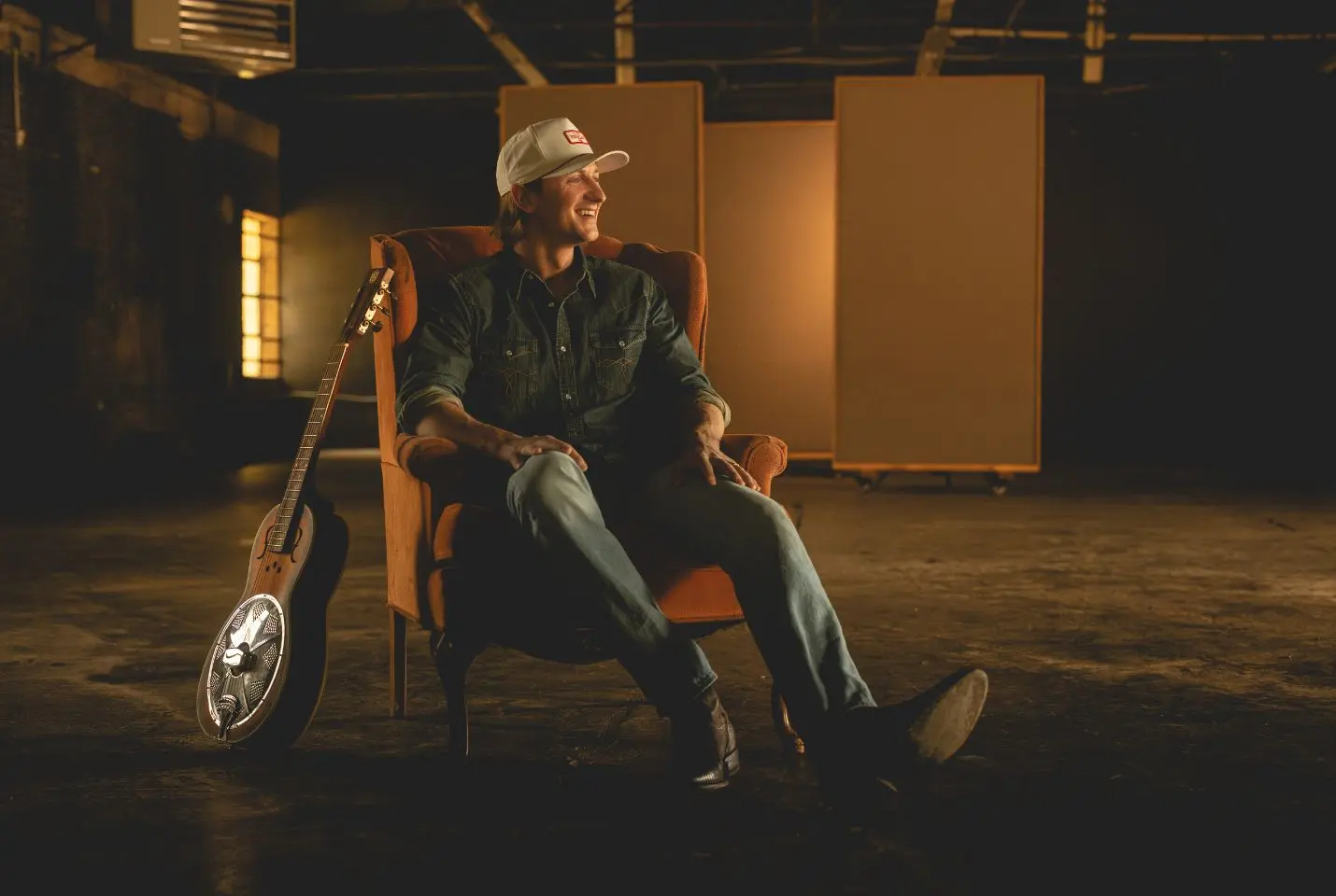 Cooper Alan sat on a chair with a guitar leaning next to him