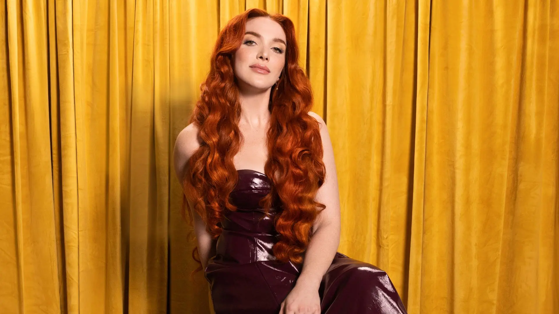 Caylee Hammack wearing a black dress sat in front of a yellow curtain