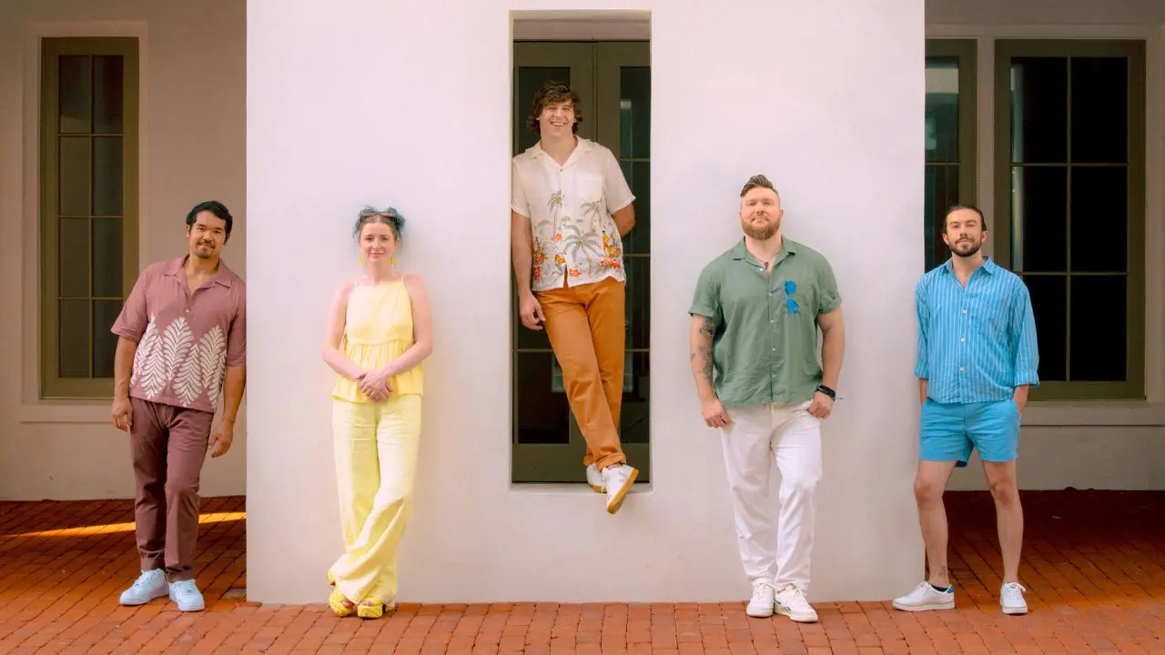 Five people stood against a white wall in brightly coloured clothing