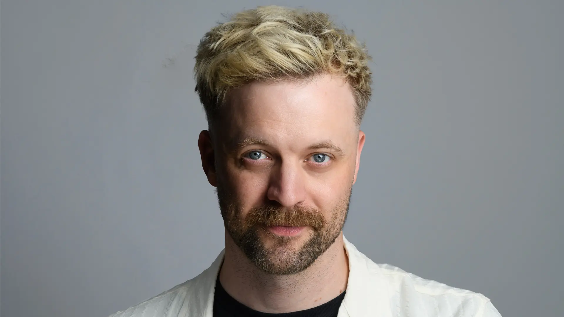 Thomas Green kijkt licht glimlachend in de camera, in een wit overhemd en zwart shirt, met een kleurrijk getatoeëerde arm.