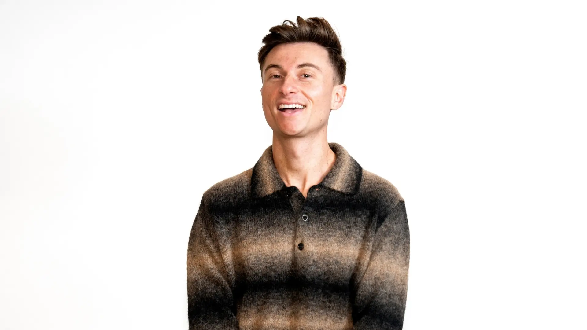 Trevor Wallace glimlacht in een studioportret tegen een lichte achtergrond, gekleed in een gestreepte trui met kraag.