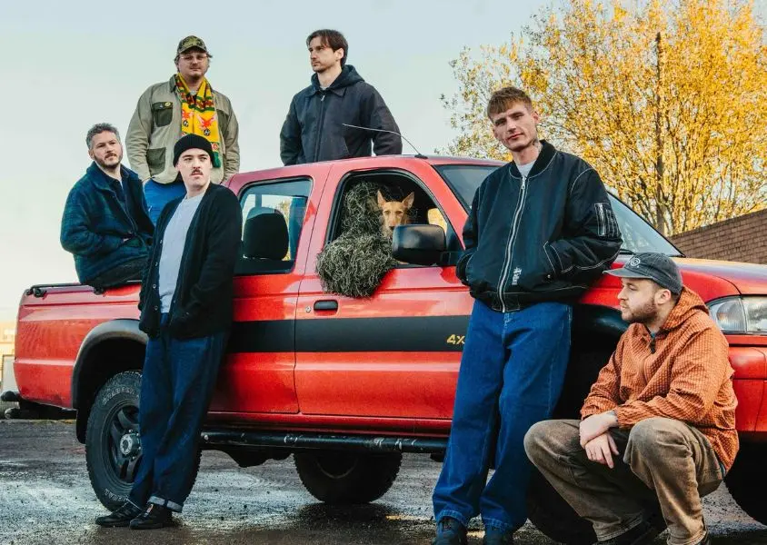 band posing next to red car