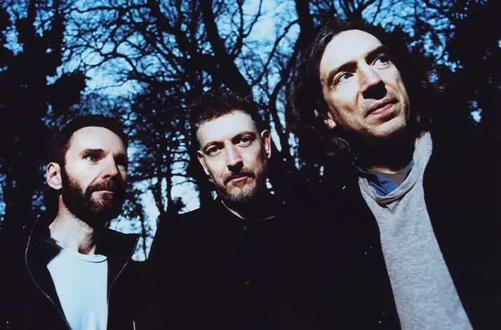 De drie bandleden van Snow Patrol naast elkaar in een bos in de schemering