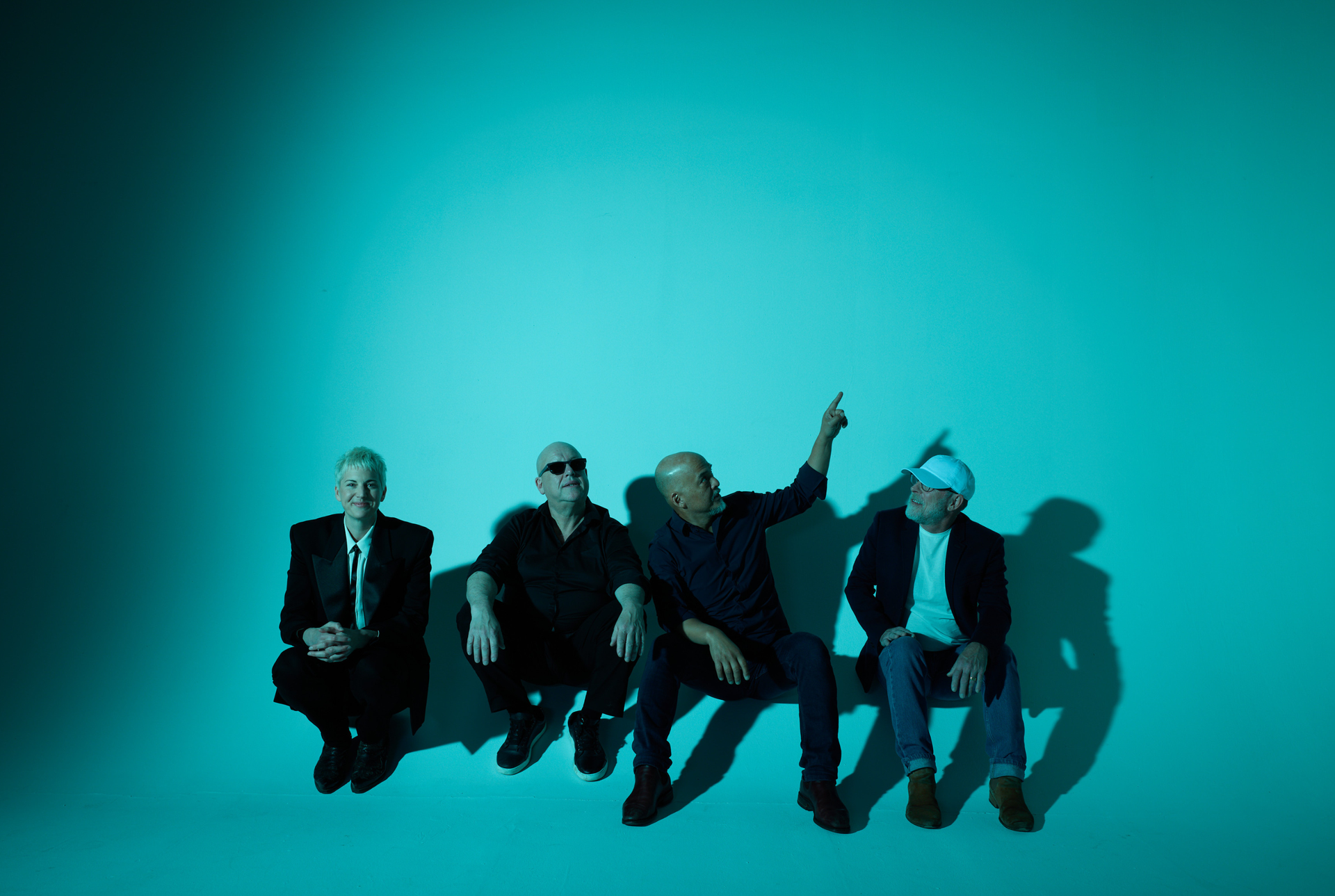 Members of the band Pixies sat on the floor of a studio in blue lighting