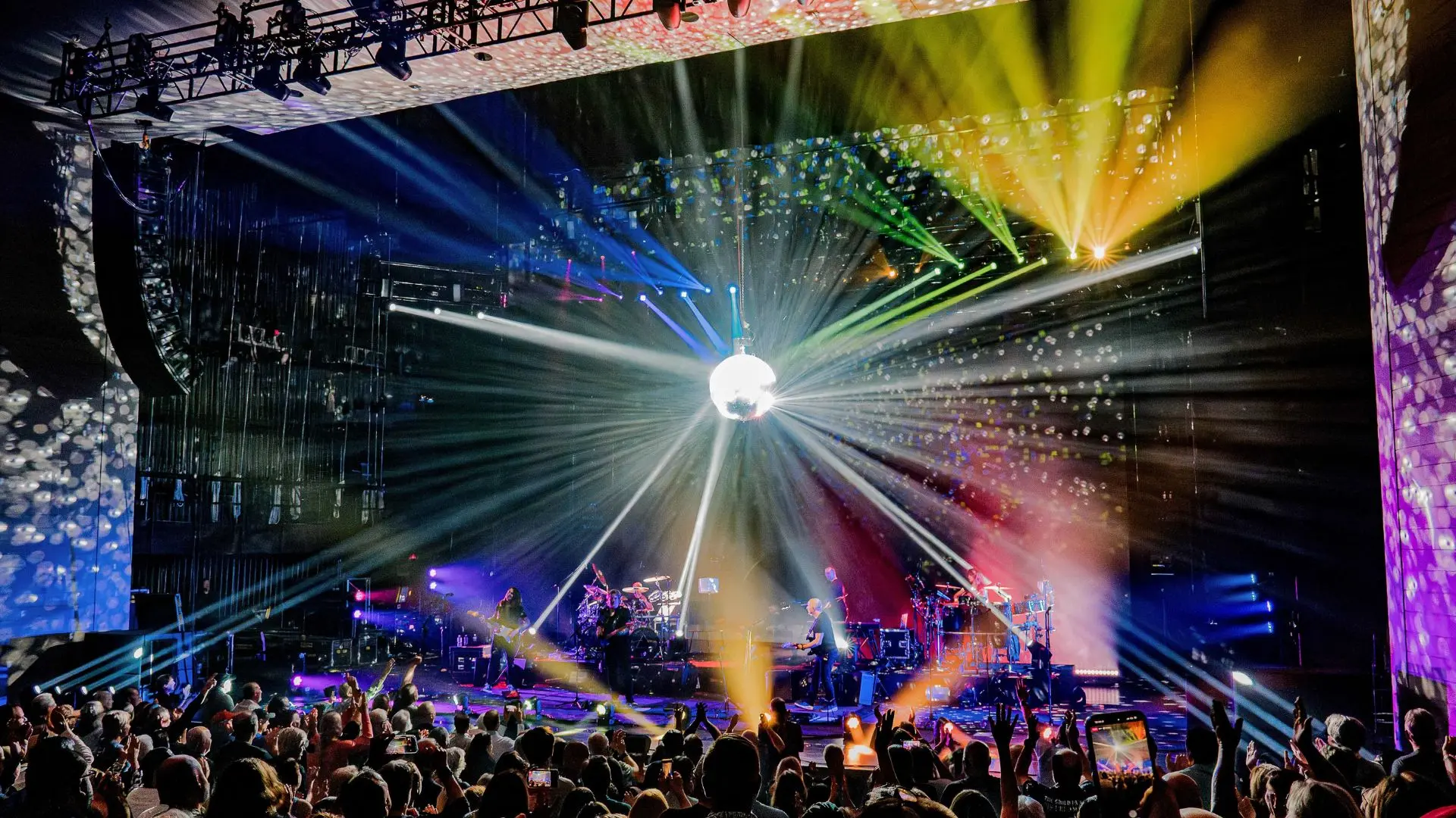 Bühne mit bunten Lichtstrahlen und Discokugel vor Publikum bei Konzert