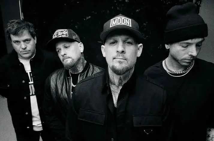 wart-wit groepsportret van de band Good Charlotte: vier bandleden staan dicht bij elkaar, deels met petten en muts, in donkere kleding en met een serieuze blik recht in of weg van de camera.