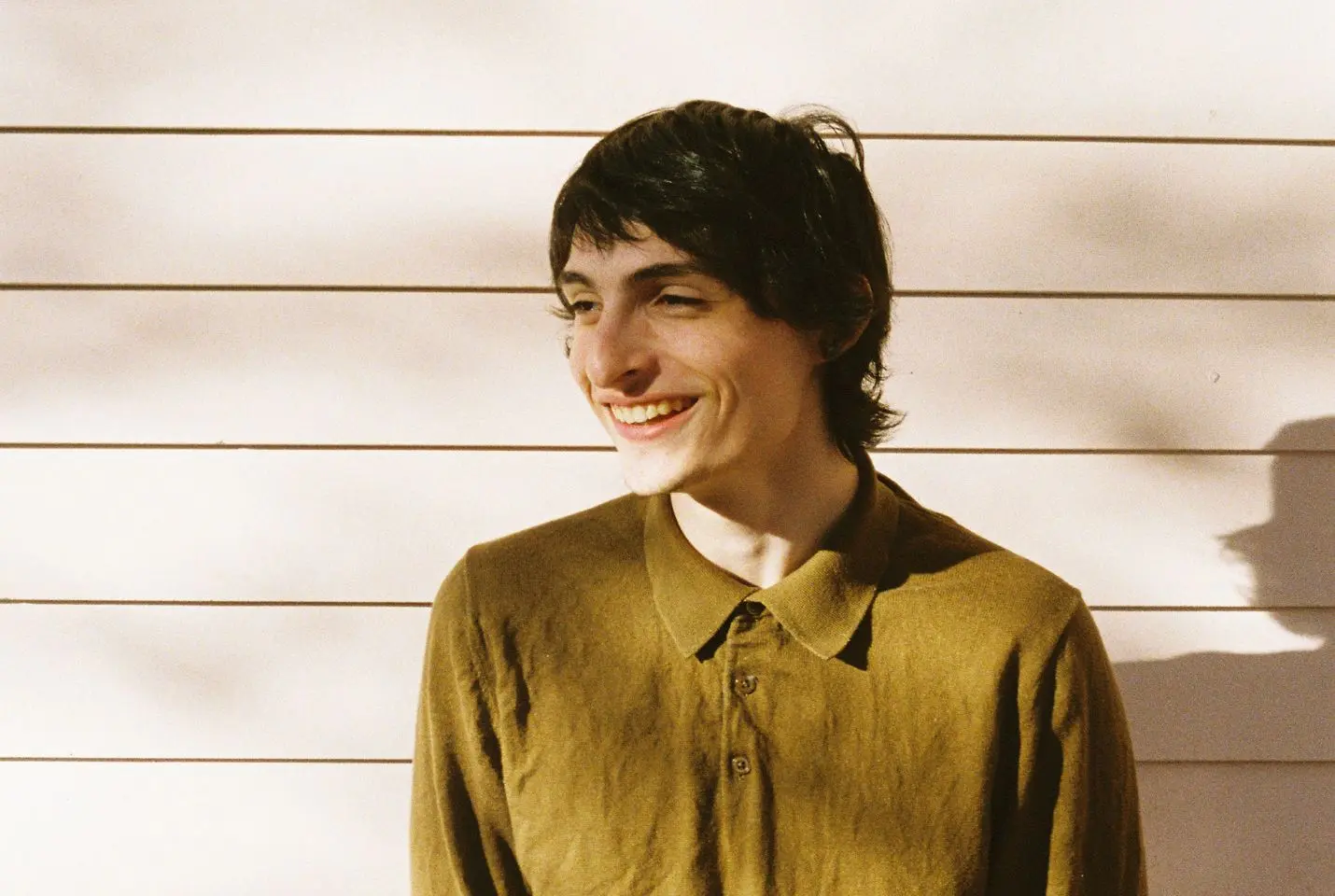 Boy smiling in green shirt against wall