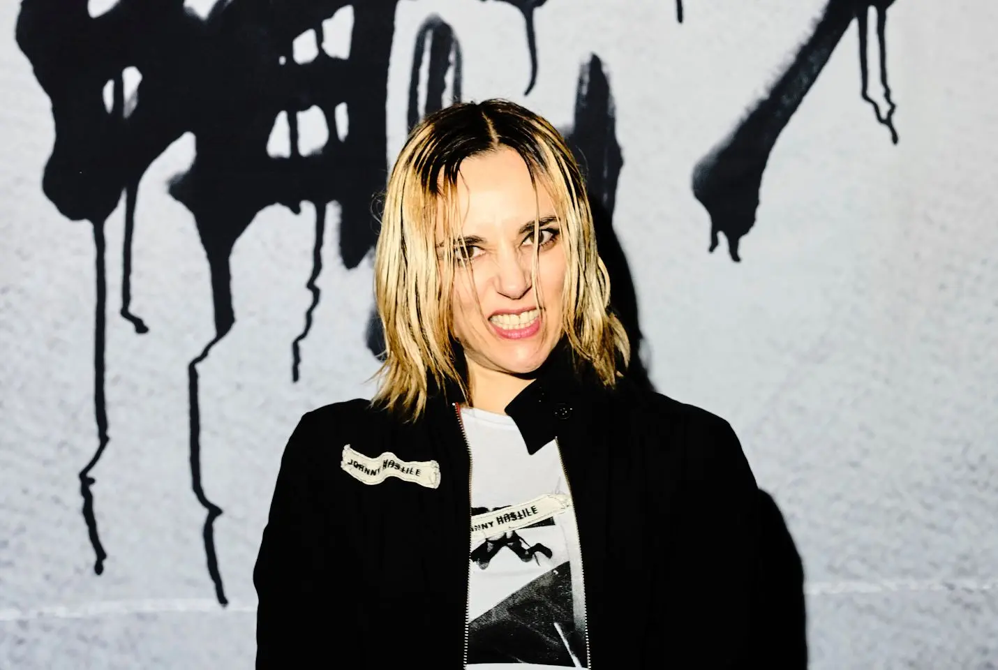 Jehnny Beth smiling in front of graffiti wall