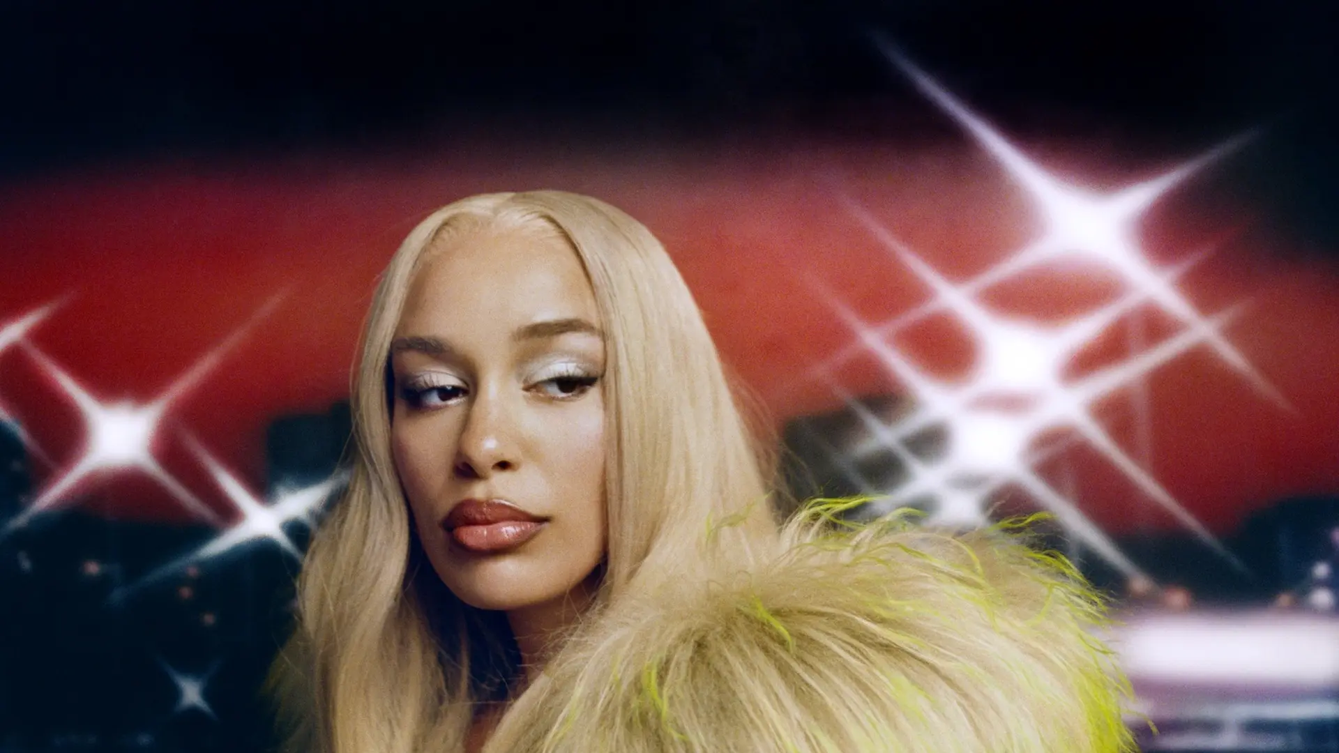 Jorja Smith kijkt opzij, met lang blond haar en een opvallende bontjas, tegen een donkere achtergrond met felle lichtflitsen.