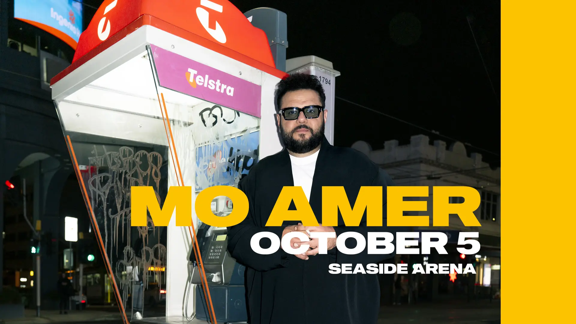 Mo Amer leant up against a phone booth in a busy city at night