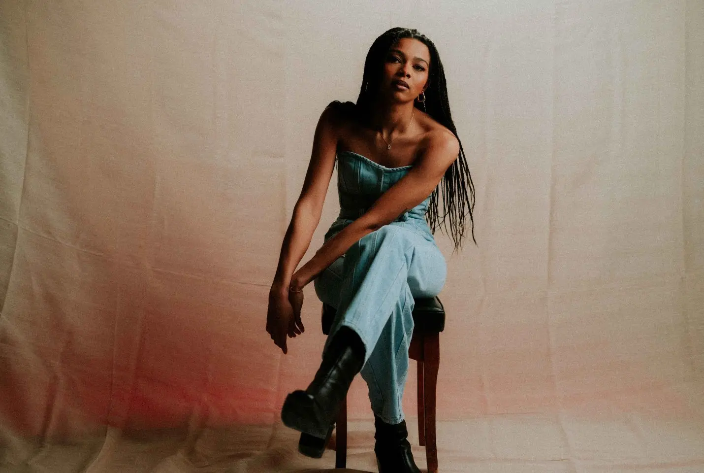 A woman wearing a denim jumpsuit sat on a stool