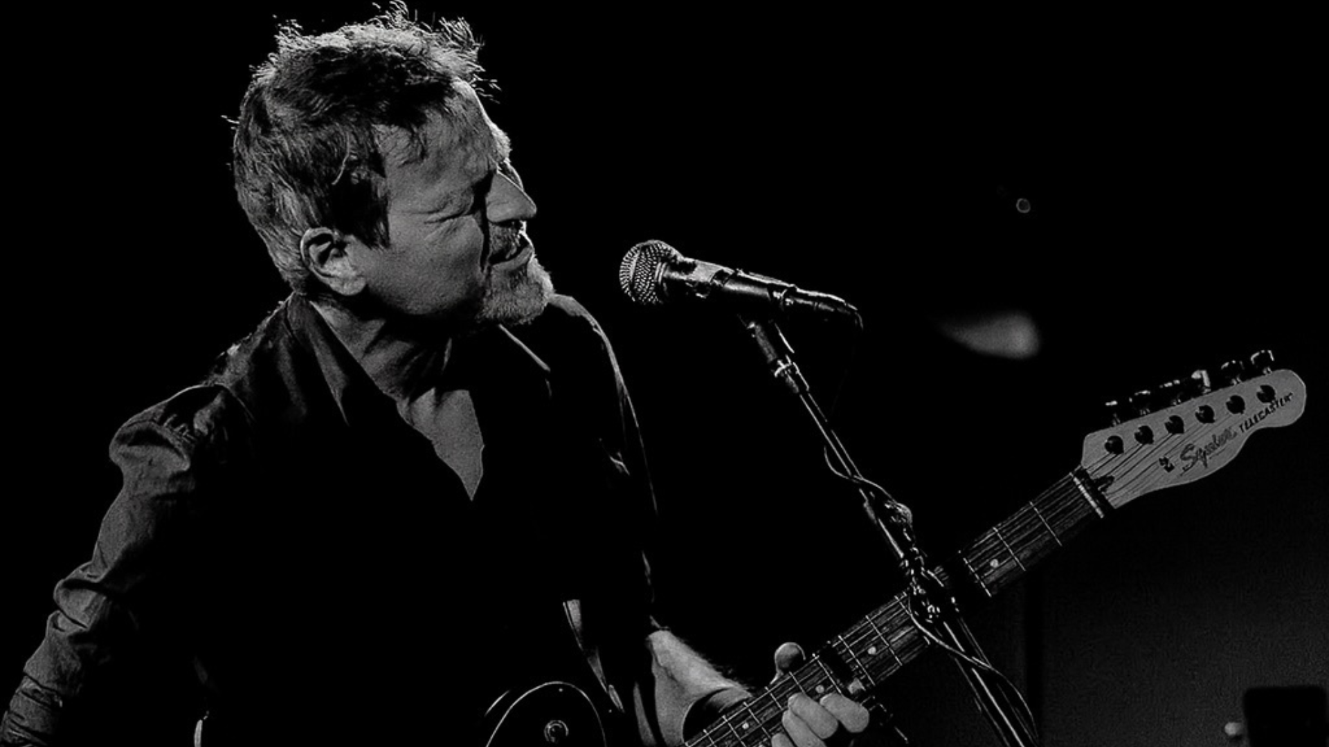 Black and white photo of singer tom mcrae with a guitar and microphone