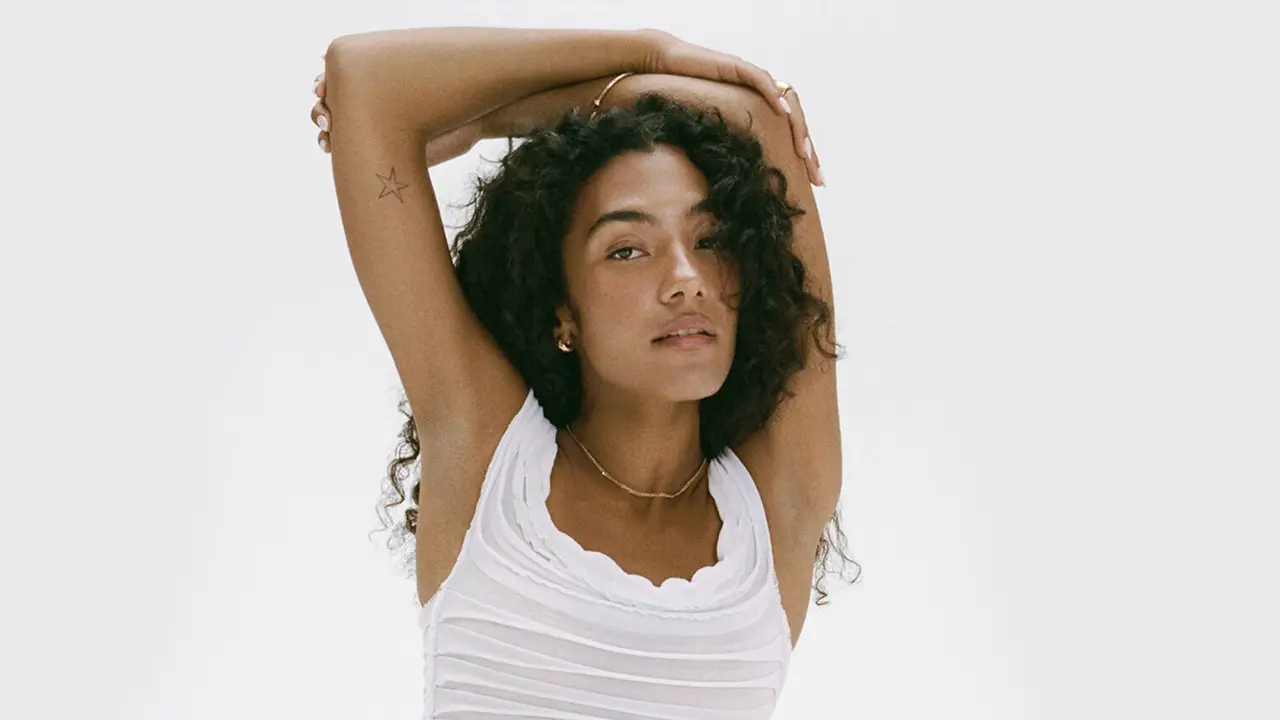 A woman wearing a white vest top with brown curly hair