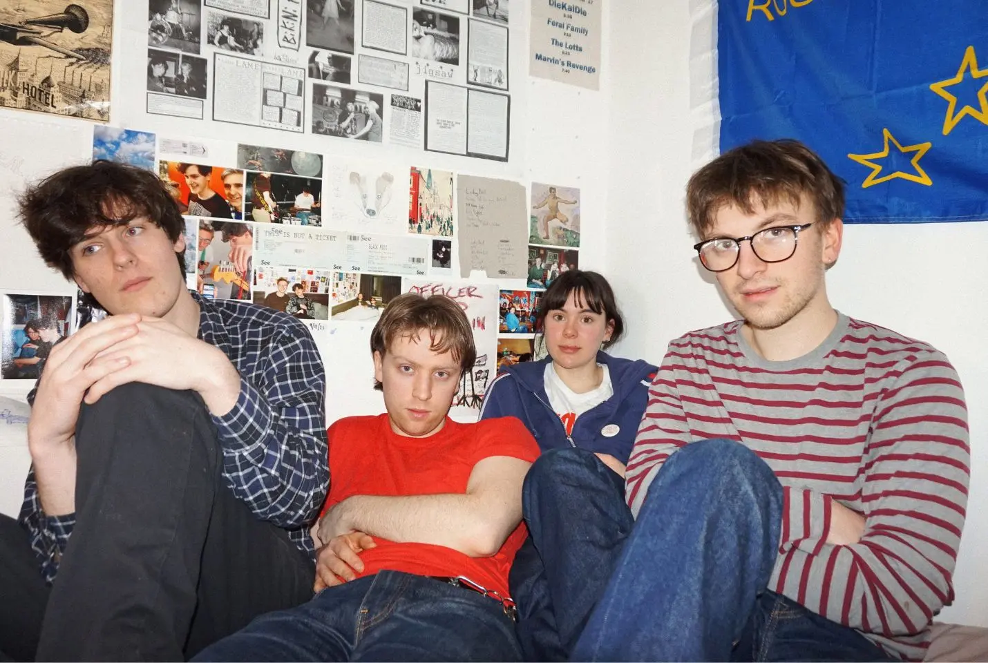 Four people sit in the corner of a room with lots of posters on the wall behind