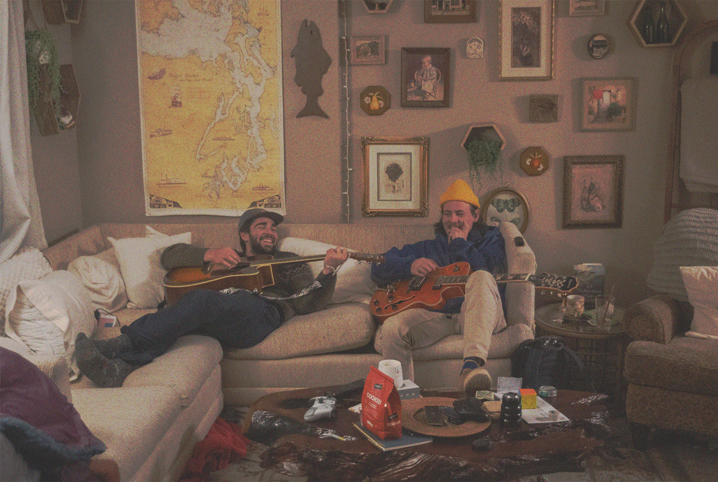 Two men sitting on couch playing guitar