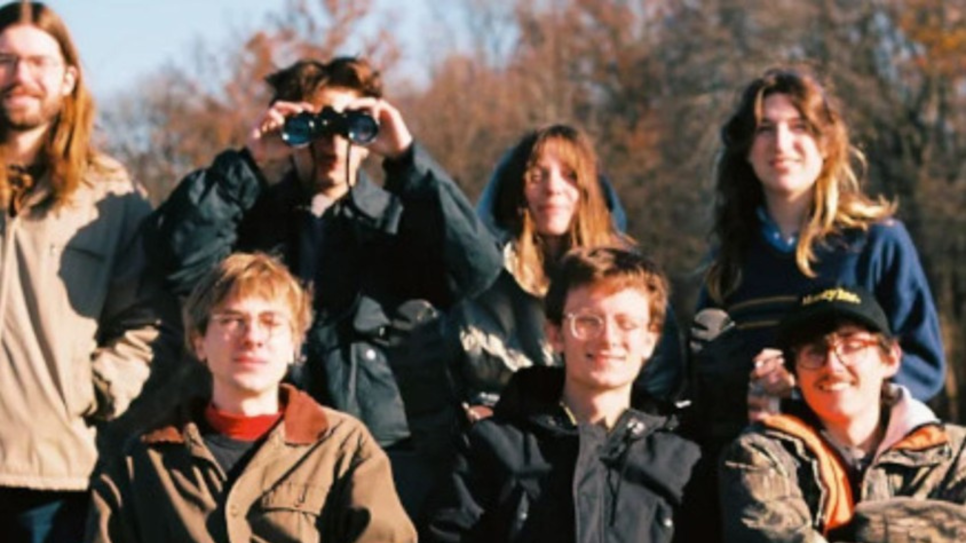 Promotional picture of Florry, the 7 members of the band are looking into the camera. One is looking through binoculars