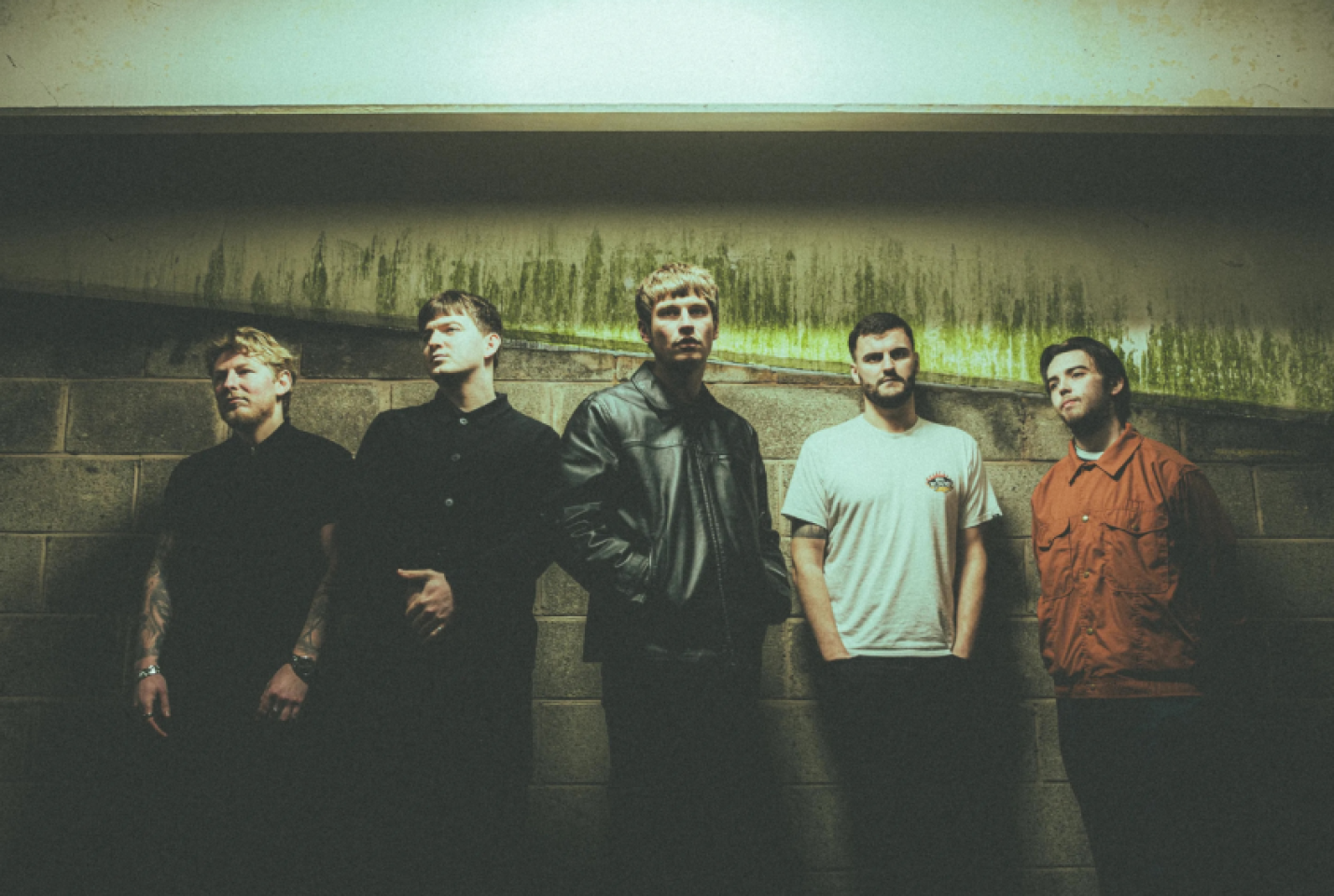 5 men posing against a brick wall