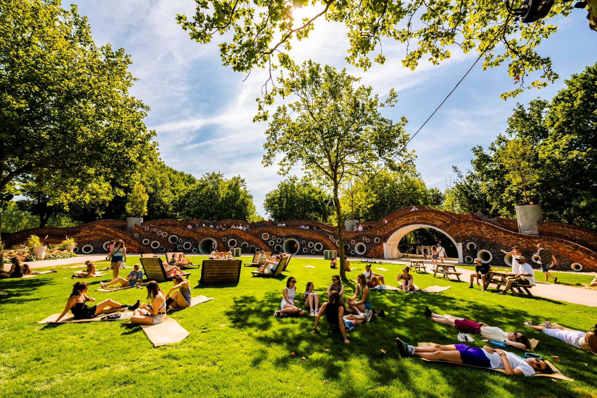 Een zomerse festivalsfeer waar bezoekers ontspannen in een heerlijk park waar ze genieten van muziek en gezelligheid.