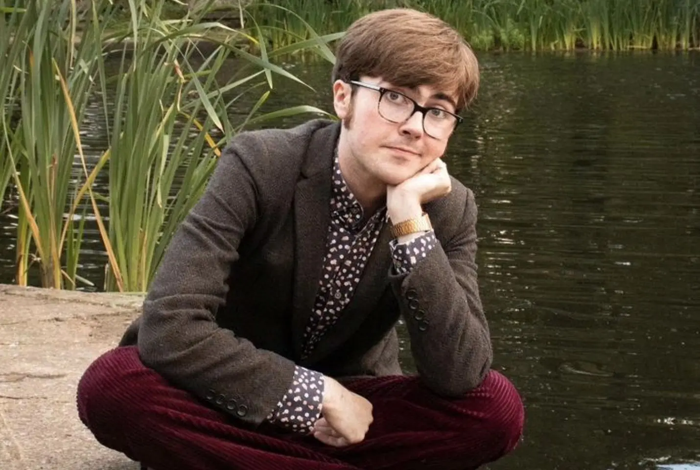Man sitting cross legged next to pond