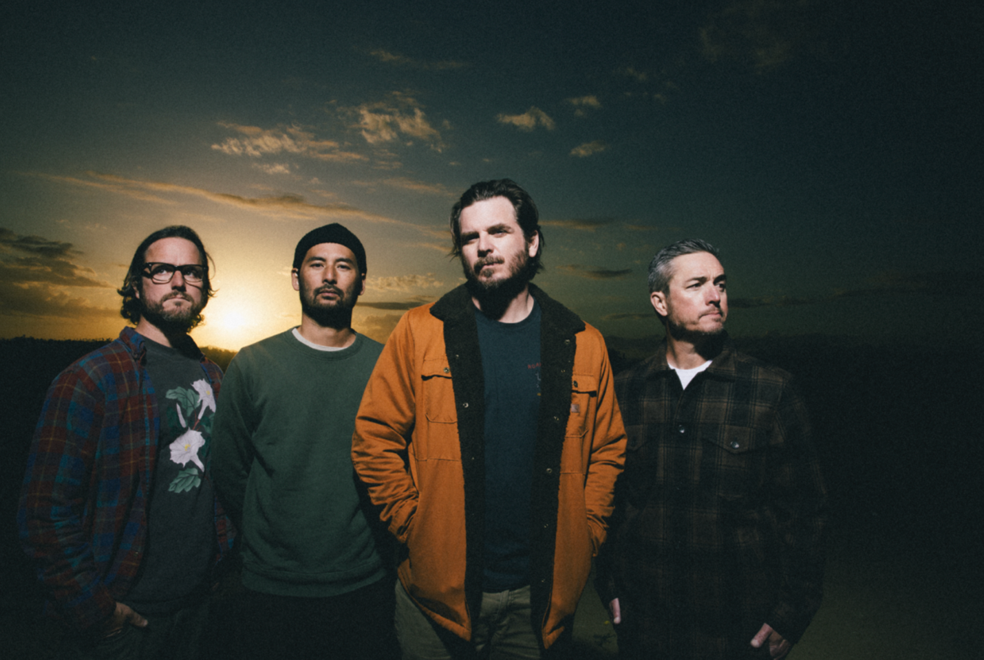 Artist Thrice standing with sunset behind them