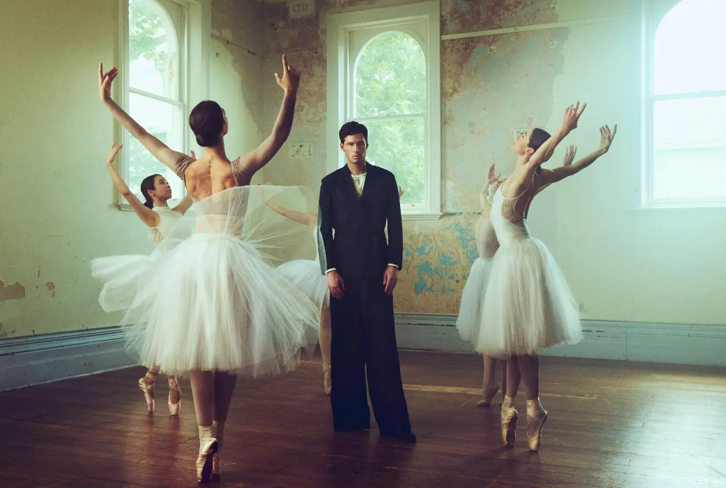 SWIM wearing a black suit surrounded by 4 ballerinas