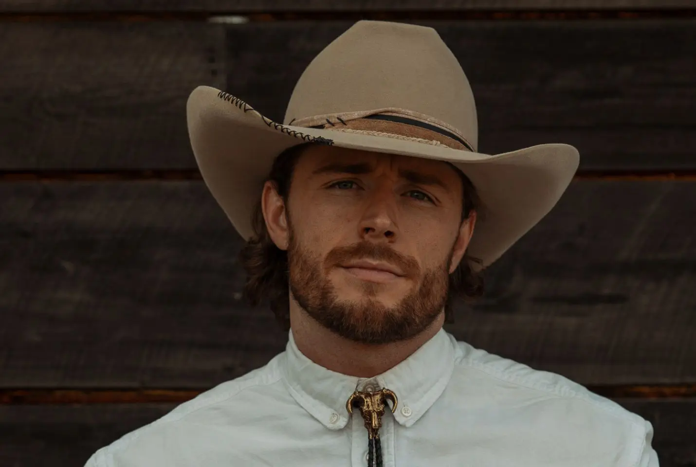 A man wearing a beige cowboy hat, white shirt, and bolo tie