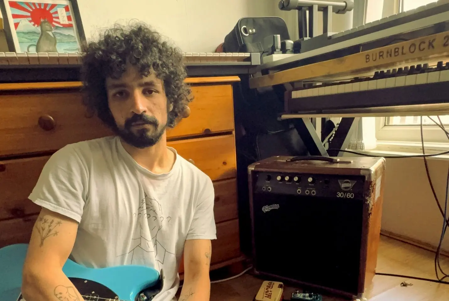 Man posing with a guitar next to a keyboard