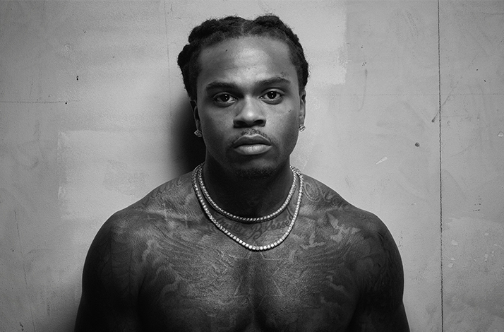 Black and white portrait of Gunna standing in front of a white wall