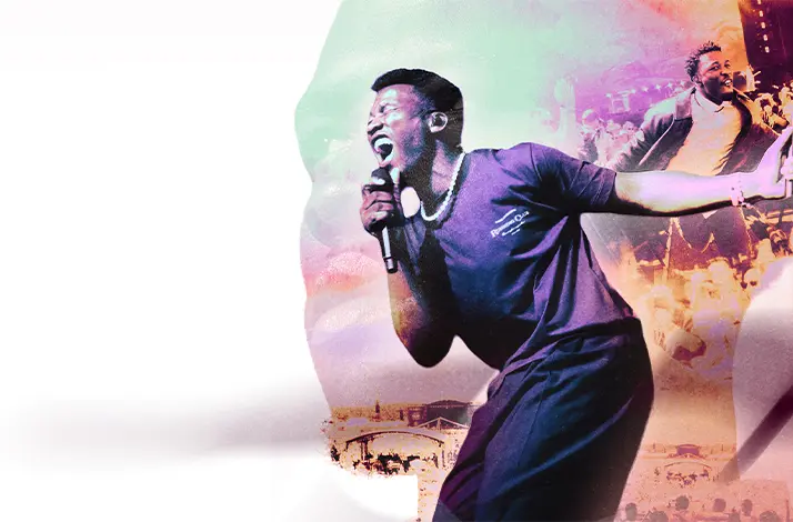 Claude staat op het podium en zingt krachtig in een microfoon, met zijn arm uitgestrekt; kleurrijke lichteffecten en een menigte op de achtergrond creëren een energieke concert­sfeer.