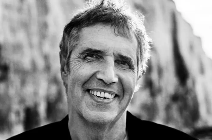 Zwart-wit portretfoto van de zanger Julien Clerc met rotsachtige kliffen op de achtergrond, sterk contrast, natuurlijke belichting en onscherpe omgeving.