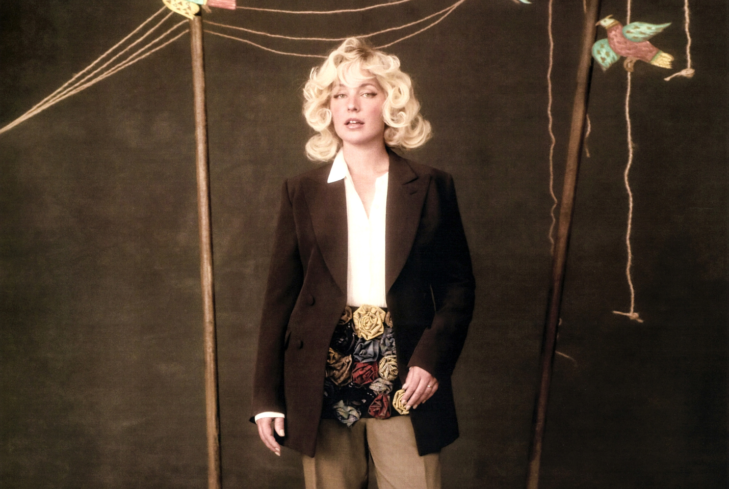 Girl with short blonde curly hair, standing against brown background