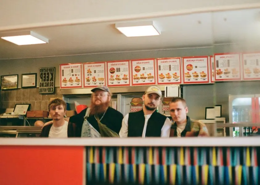 Promotional shot of the band Skustin standing behind a fast food counter