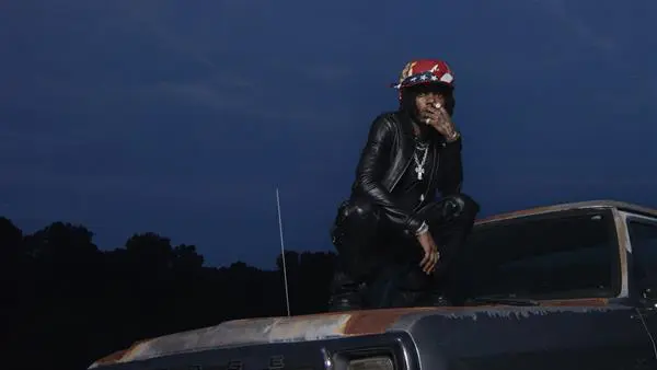 JID sitting on the hood of a car