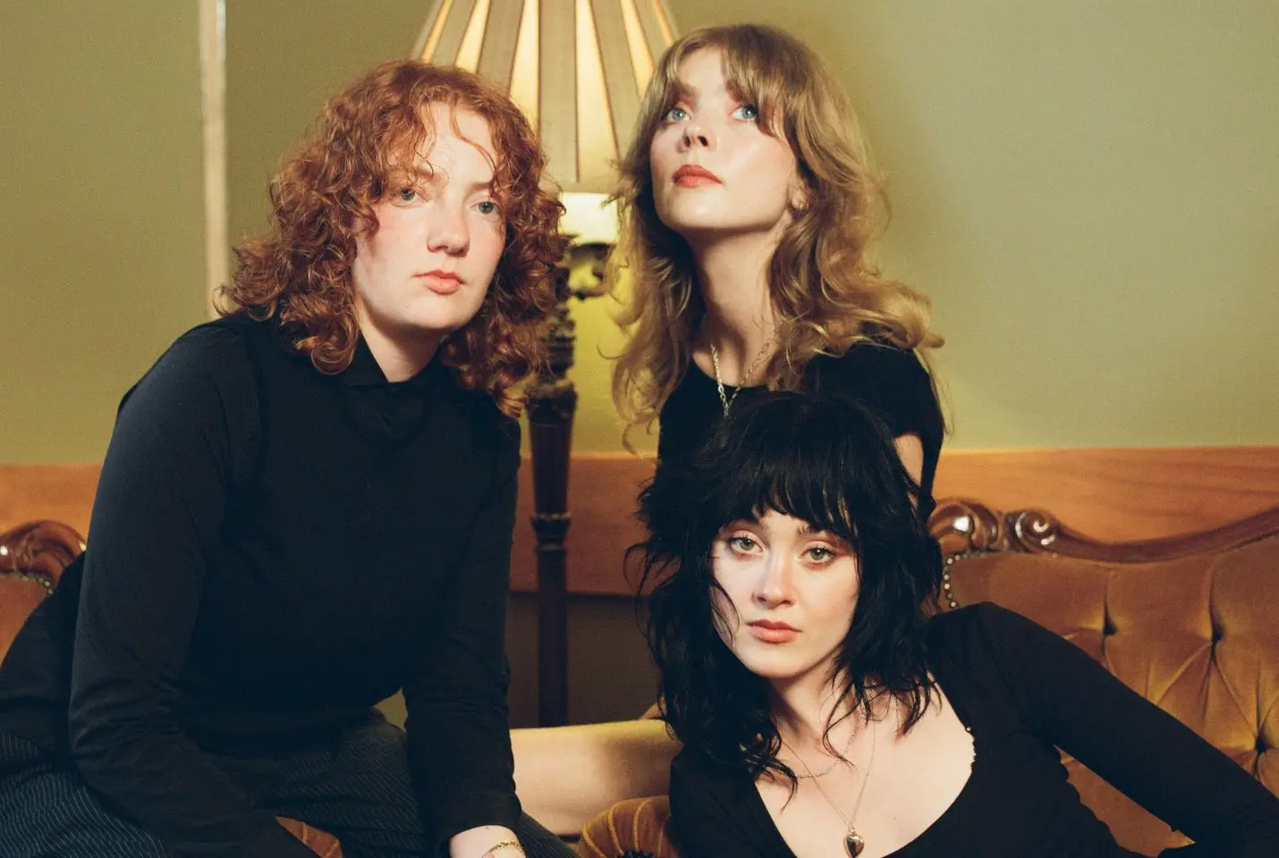Three people dressed in black sat together on a green coach