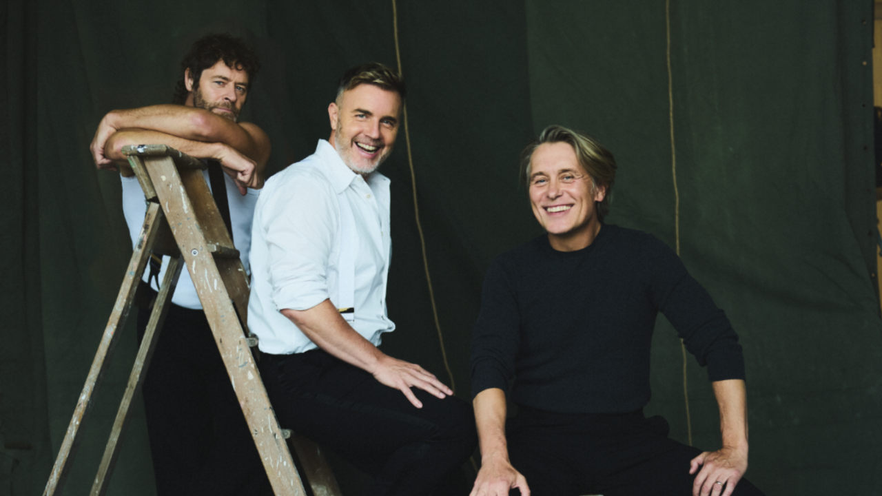 Three members of take that sat on a paint-stained ladder in front of a dark background