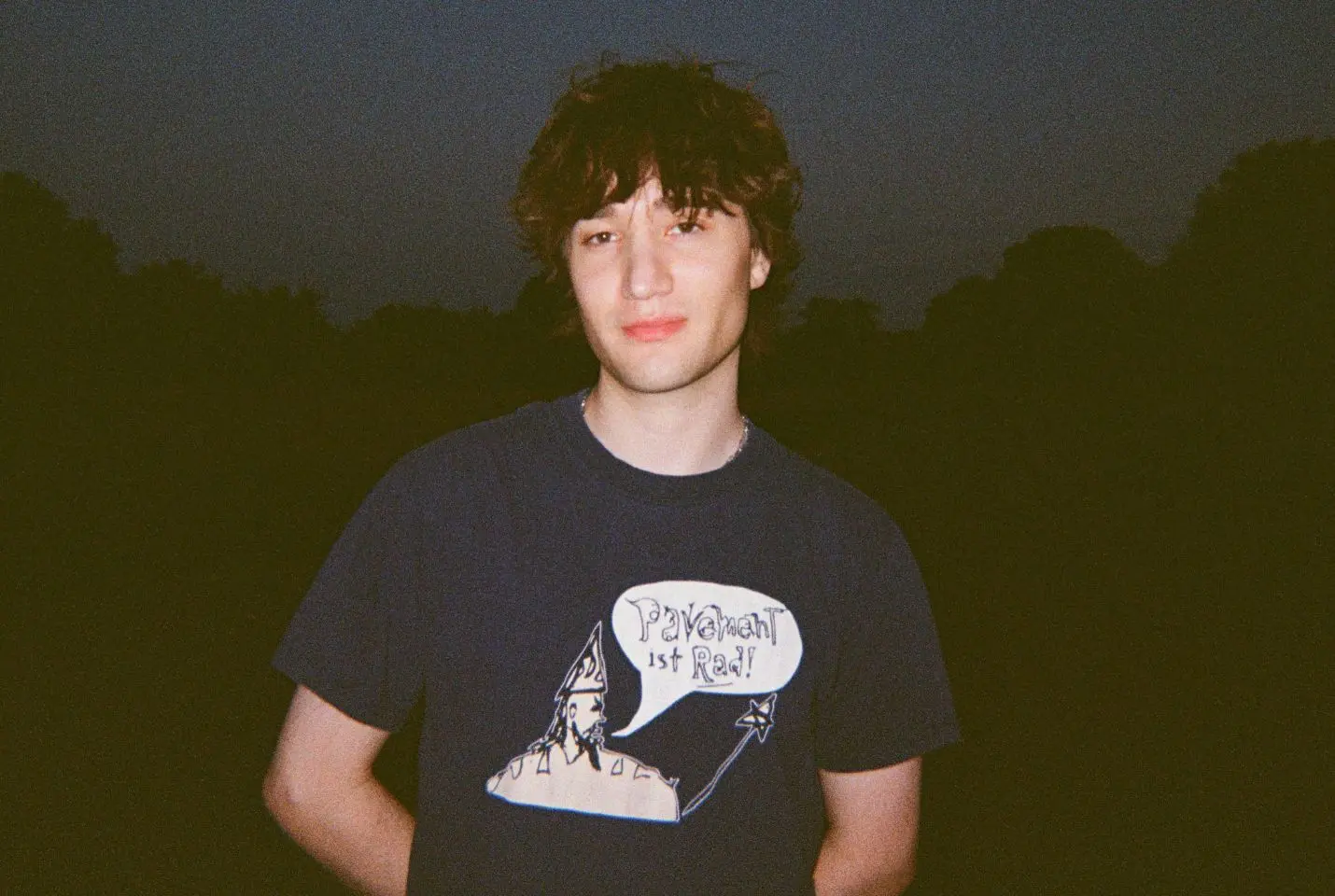 A man with messy short brown hair wearing a navy tshirt