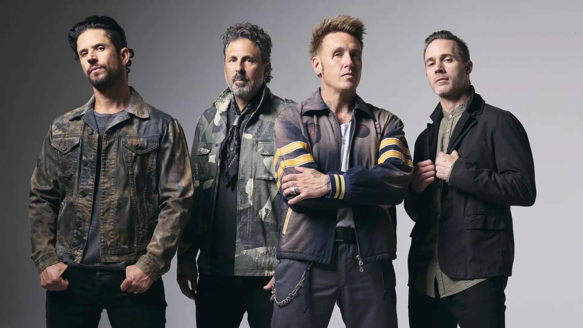 De band Papa Roach poseert in een studio tegen een lichte achtergrond, met vier bandleden die recht in de camera kijken.