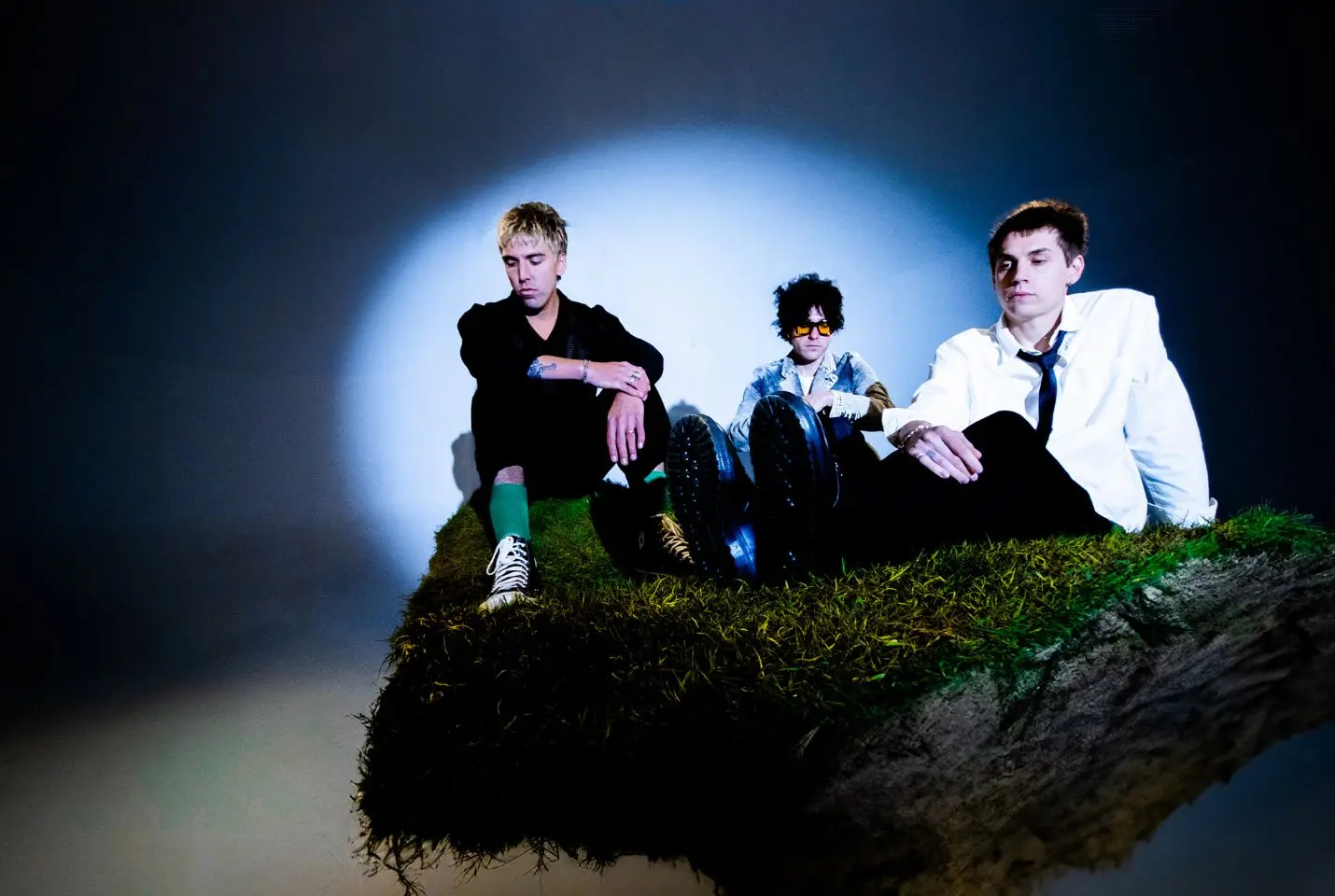 3 men posing on top of a mossy rock with spotlight on them