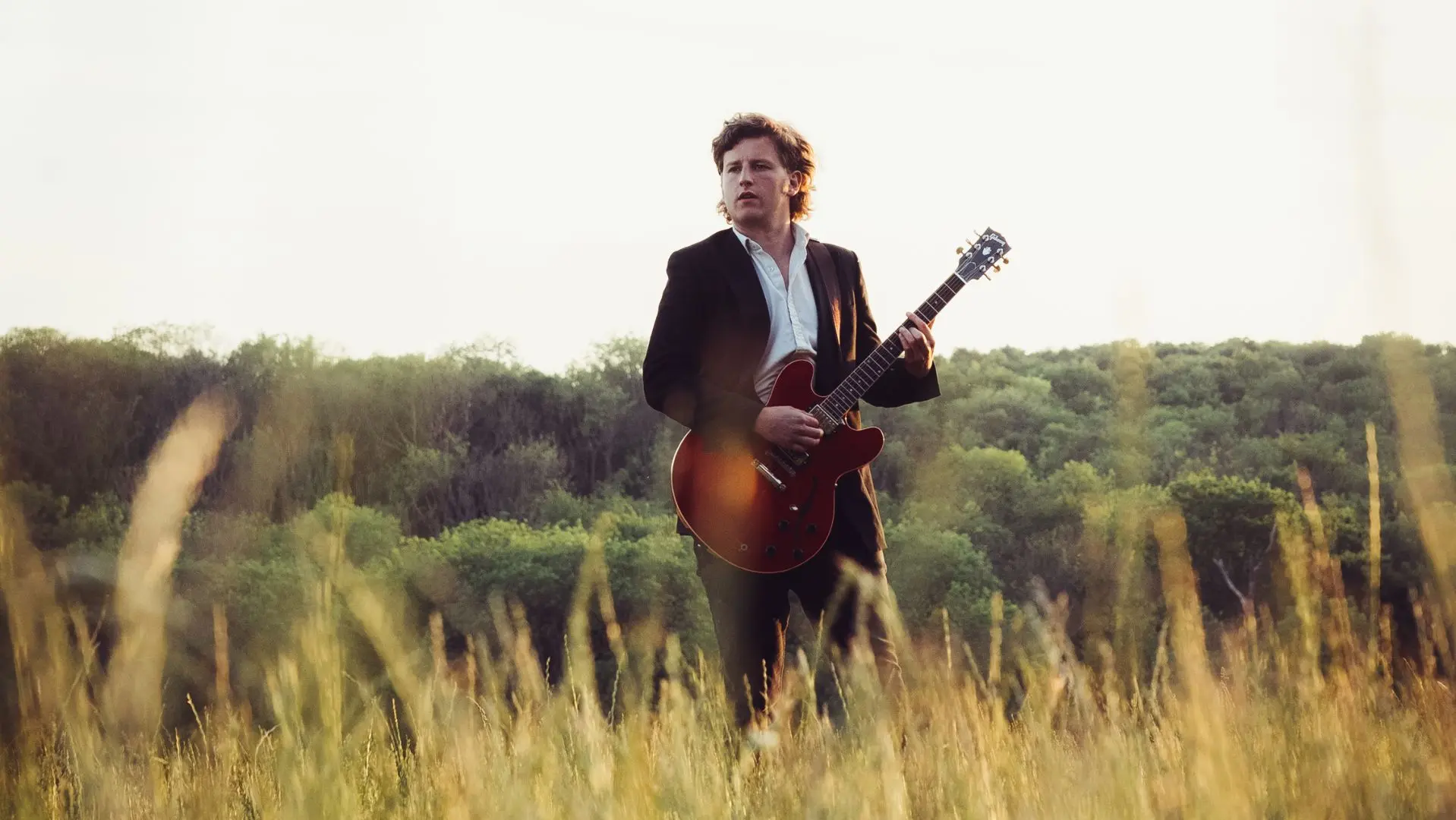 Weston Loney holding a guitar stood in a field