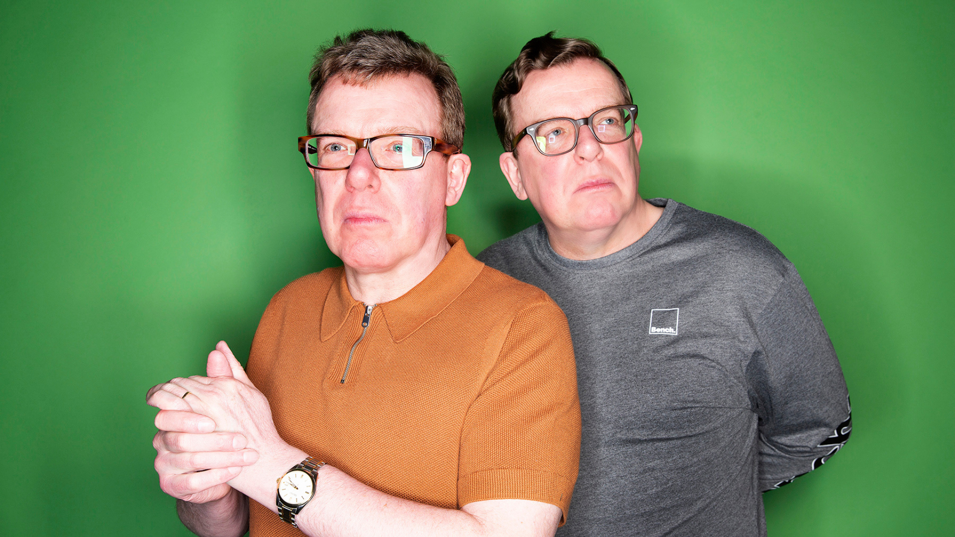 The proclaimers promotional picture, two men standing infront of a green background.