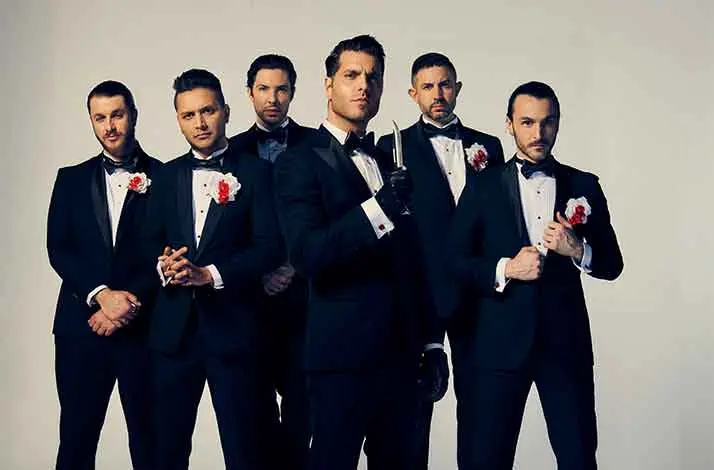 Vijf bandleden van Ice Nine Kills poseren in zwarte smoking met rode bloem op de revers. Frontman Spencer Charnas staat in het midden en draagt een zwarte handschoen en houdt een mes vast, wat een stijlvolle, horrorachtige sfeer oproept.